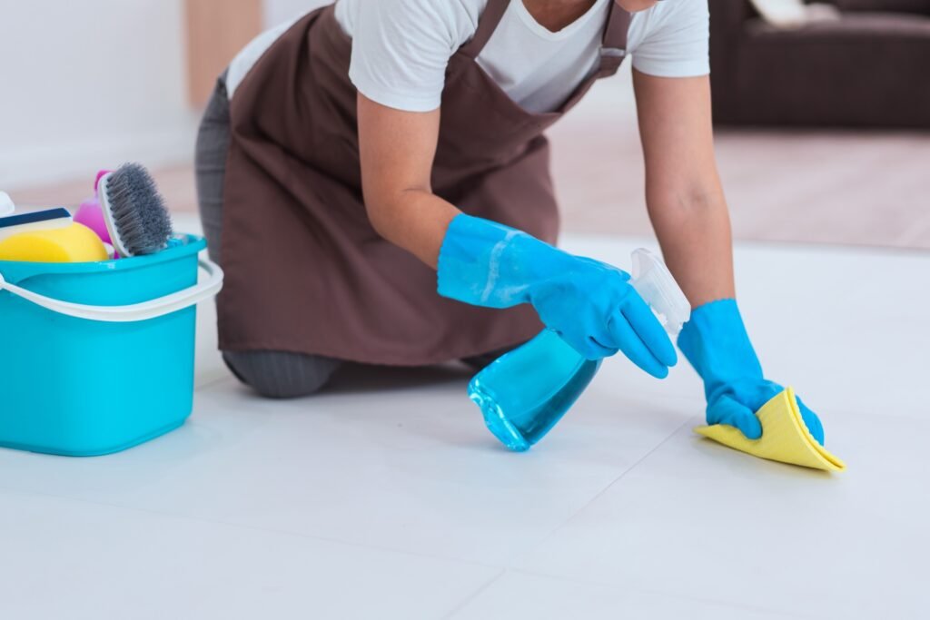 Maid wearing gloves and using cleaner spray and microfiber cloth to wipe a dust on the floor