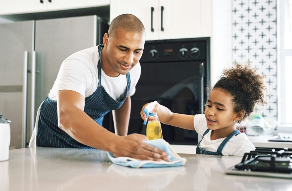 Shot of a young man cleaning a surface with a child at home