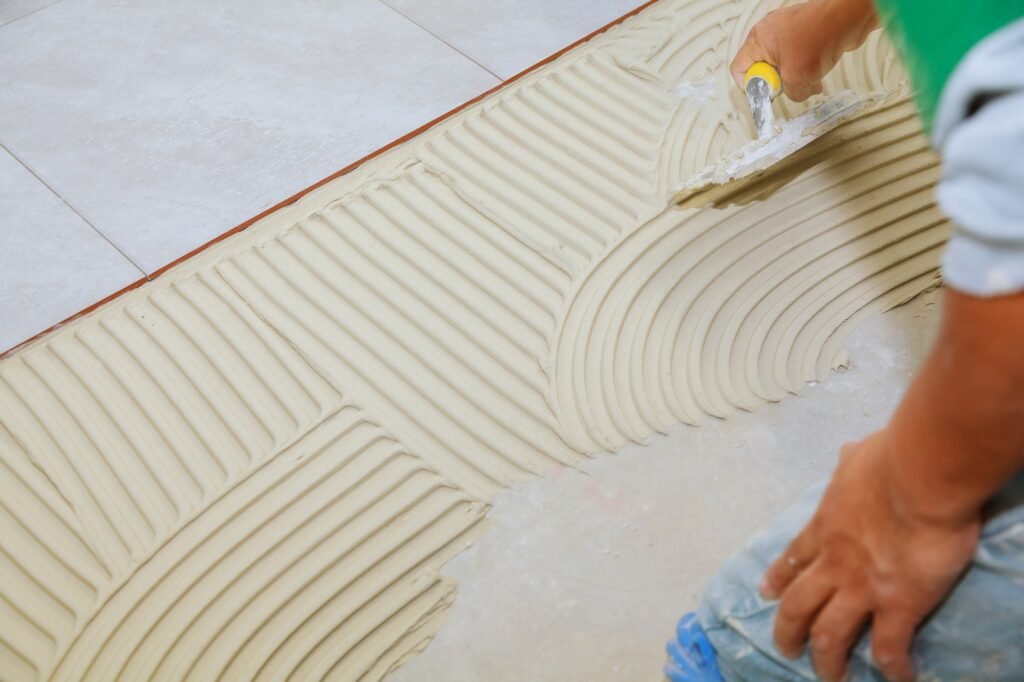 Spreading wet mortar before applying tiles on bathroom floor. puts adhesive