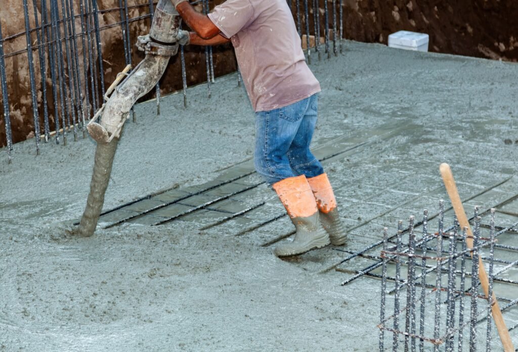 Construction worker pouring concrete into foundation with concrete pump