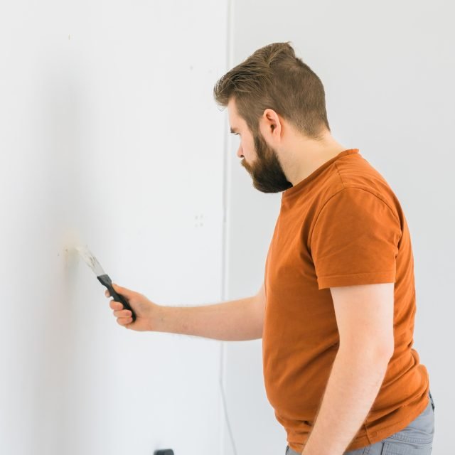 Man smoothes wall surface with a wall grinder. Male grind a white plaster wall - renovation and